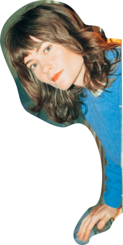 A cutout of Rowena Wise pokes her head out from the side of the screen. She has a slight, curious smile on her face. She is wearing a bright blue sweater and red lipstick.